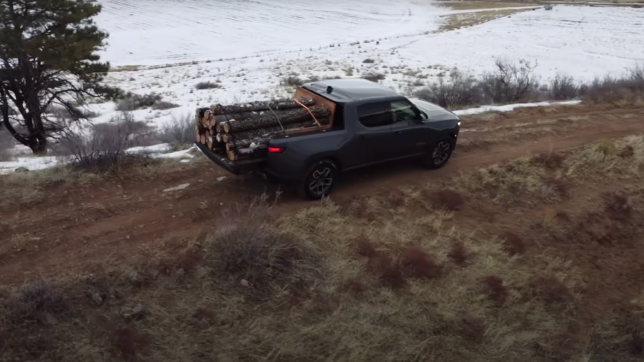 Rivian electric truck hauling a load of logs down the side of a snowy mountain.