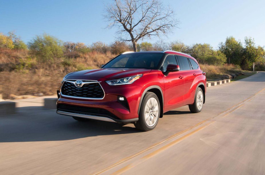 Promo photo of a red Toyota Highlander hybrid SUV driving down a remote road, trees visible in the background.