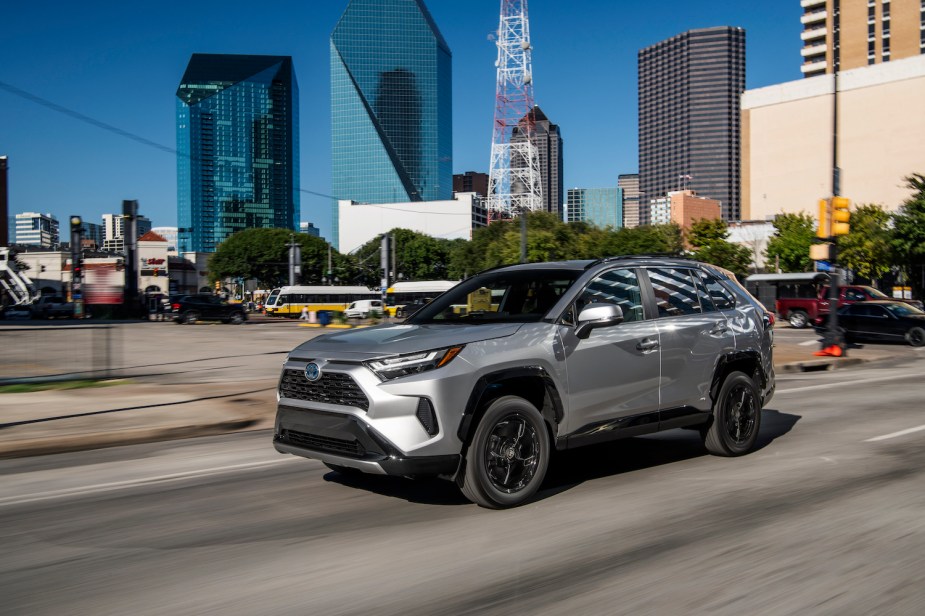 Silver Toyota RAV4 hybrid SUV driving through a downtown city center for a promotional photo. 