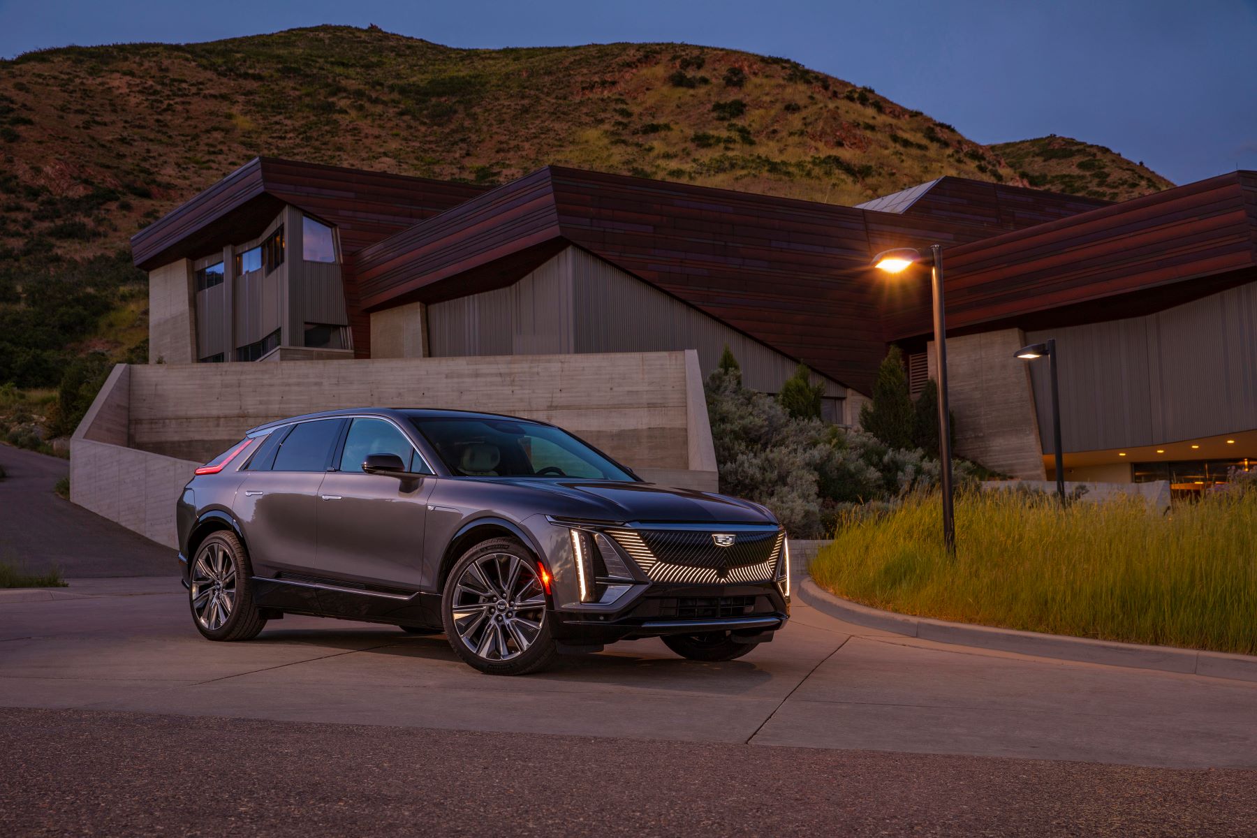 A 2023 Cadillac Lyriq luxury electric SUV parked outside a luxury home under a lamp post/streetlight