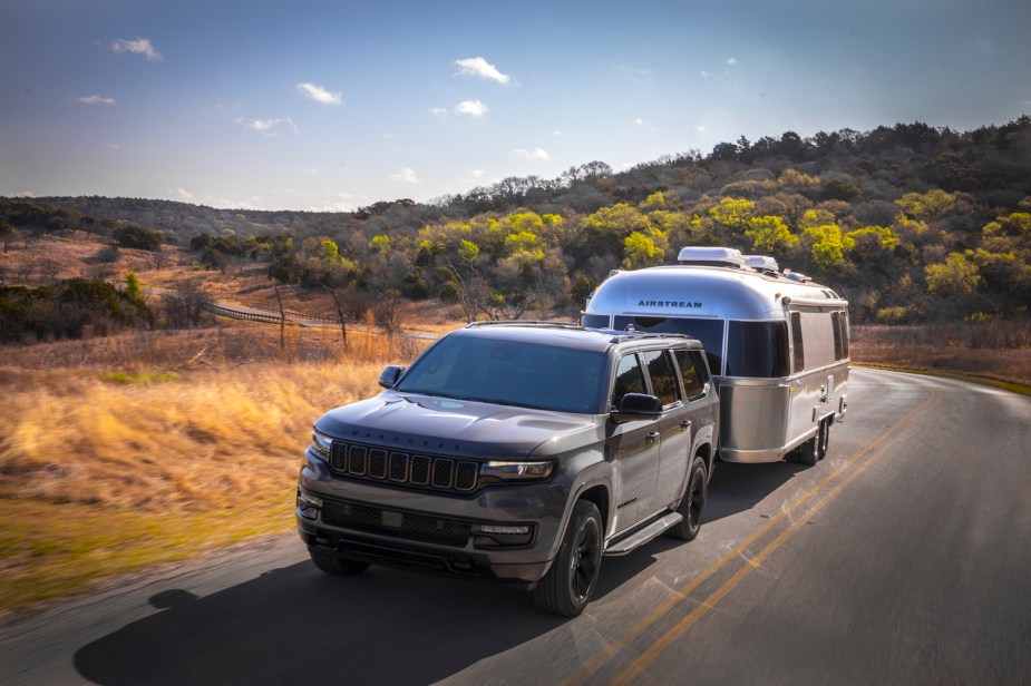 Jeep Wagoneer mild hybrid SUV shows off its towing capacity by pulling an Airstream trailer up a steep hill, trees visible in the background.