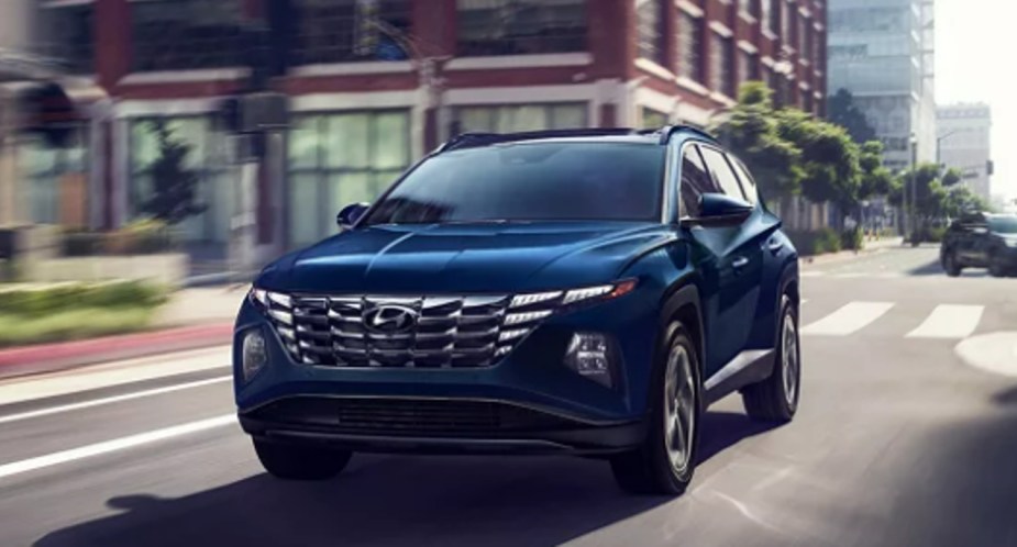 A blue 2023 Hyundai Tucson Hybrid small SUV is driving on the road.
