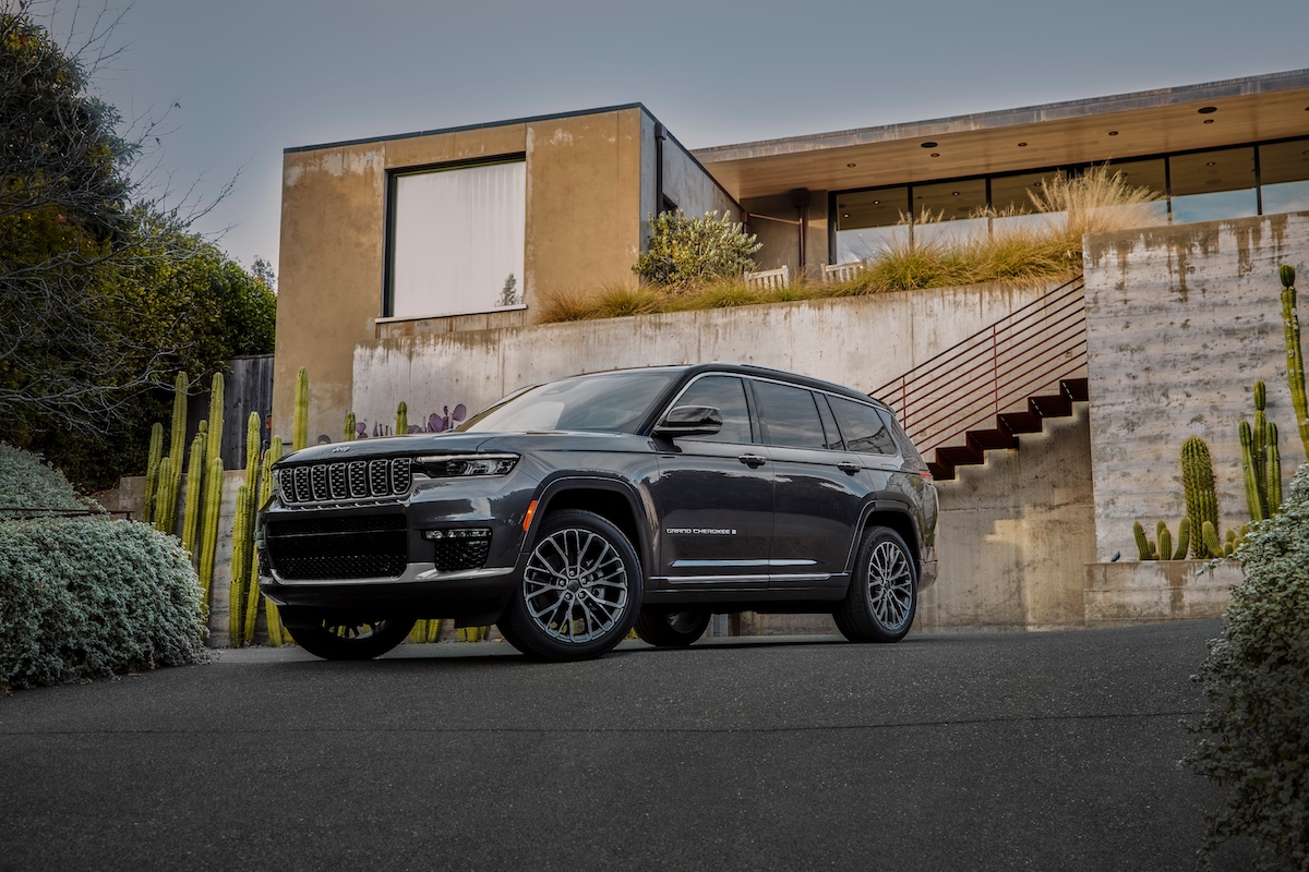 A dark colored 2023 Jeep Grand Cherokee L parked in front of a squared-off home. The L version seats seven. 