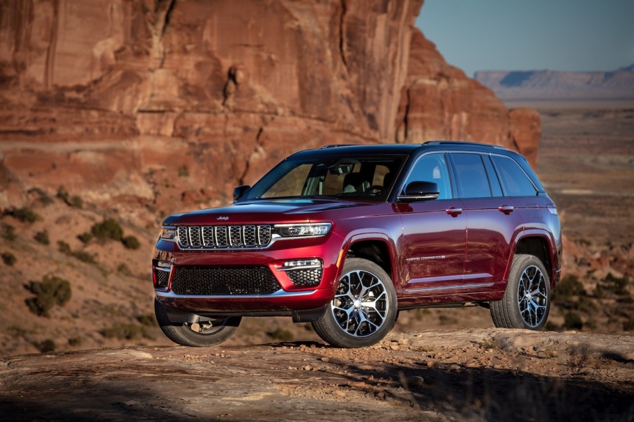 A red 2023 Jeep Grand Cherokee drives in a desert-like area.