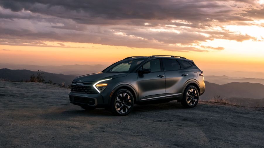 A 2023 Kia Sportage PHEV compact SUV parked on a sandy cliff at sunset with its headlights on