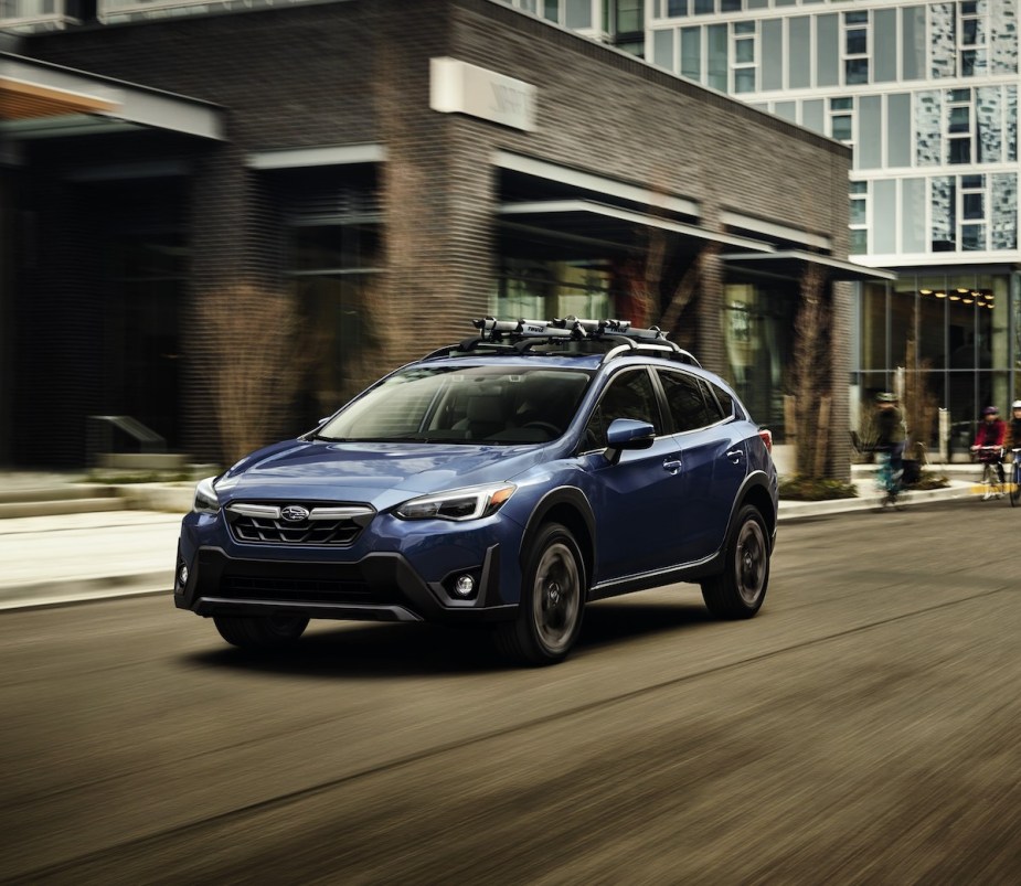 A blue 2023 Subaru Crosstrek driving down a city street surrounded by buildings.