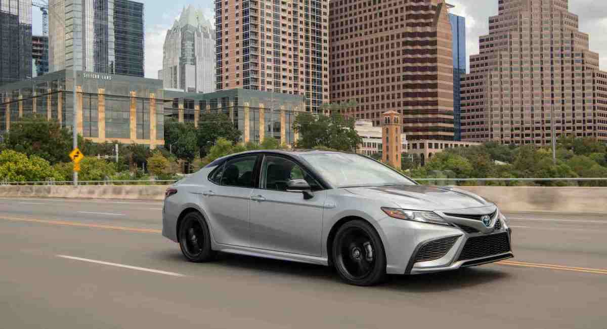 A silver 2023 Toyota Camry XSE Hybrid driving in a city