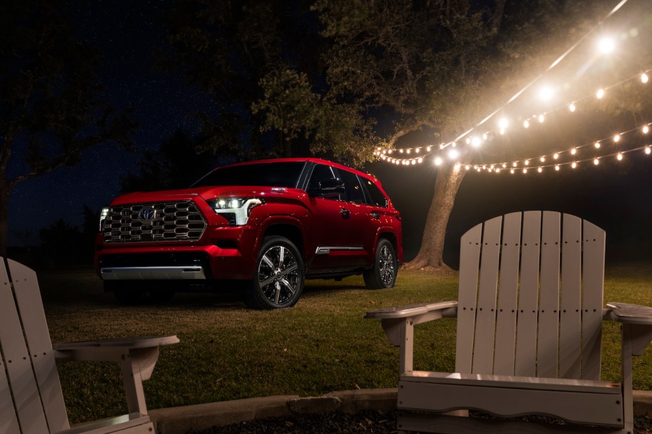 A red Toyota Sequoia hybrid SUV parked on a lawn, under a string of lights.
