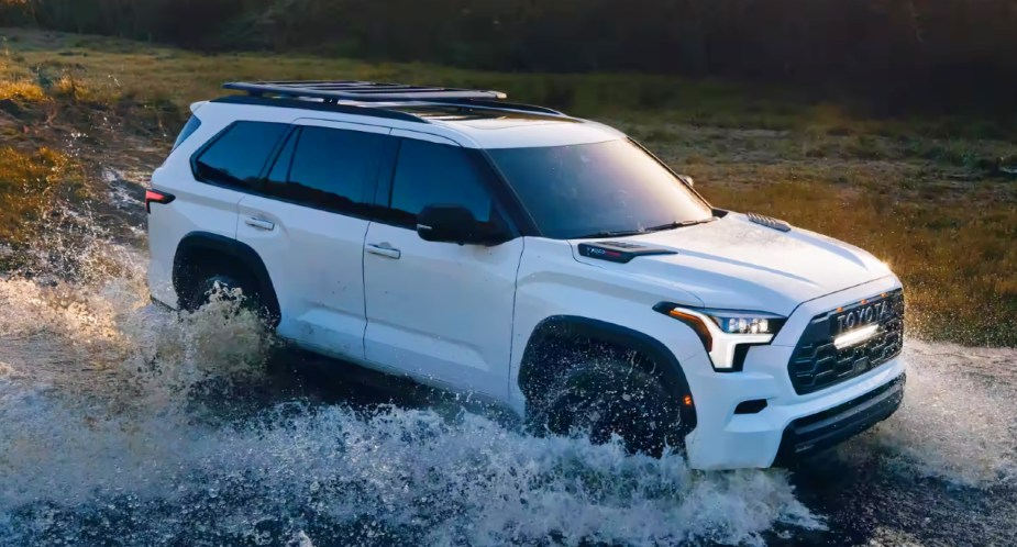 A white 2023 Toyota Sequoia full-size SUV is driving through water. 