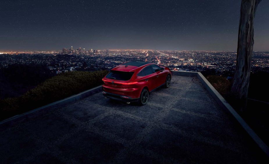 Red Toyota Venza hybrid SUV parked on a hilltop overlooking a city's night-time skyline.