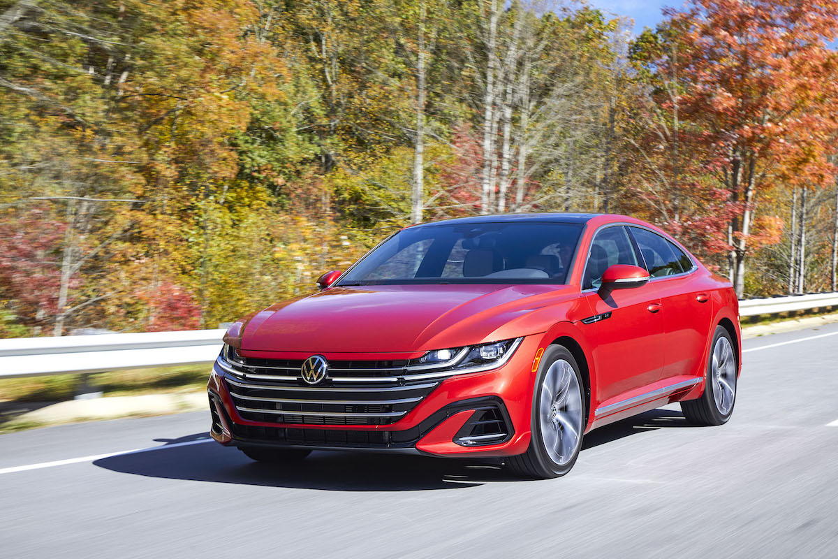 A red 2023 Volkswagen Arteon driving down a highway in a wooded area.