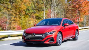 A red 2023 Volkswagen Arteon driving down a highway in a wooded area.