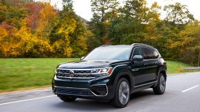 A dark colored 2023 Volkswagen Atlas driving down a road in a wooded area.