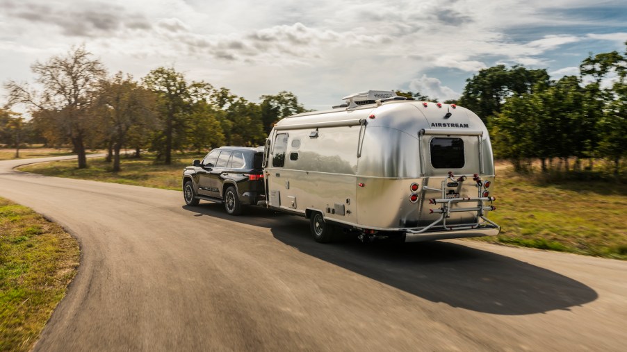 A 2023 Toyota Sequoia full-size SUV pulling an airstream camper trailer down a rural road.