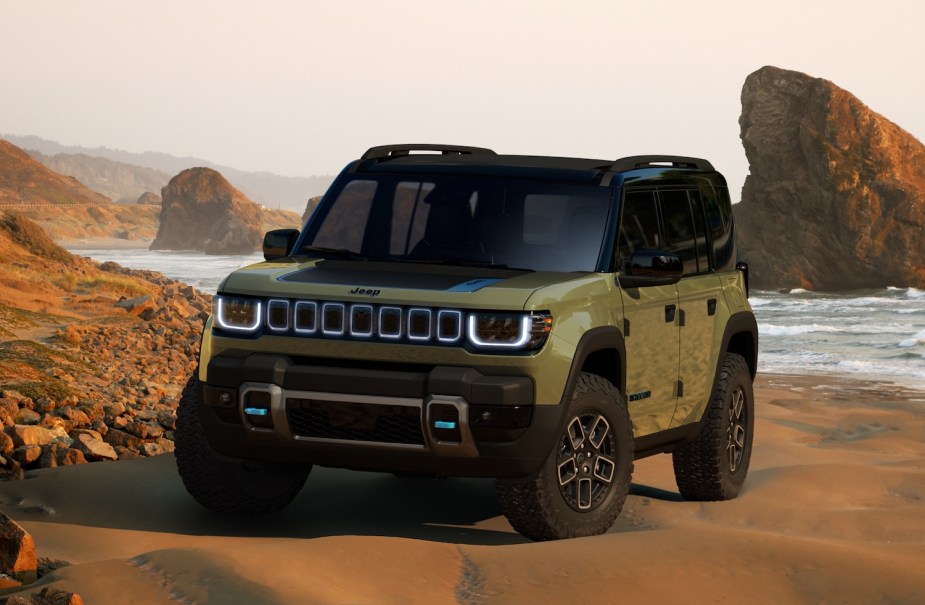 Render of a green Jeep Recon prototype electric SUV parked on a beach, rocks and waves visible in the background.