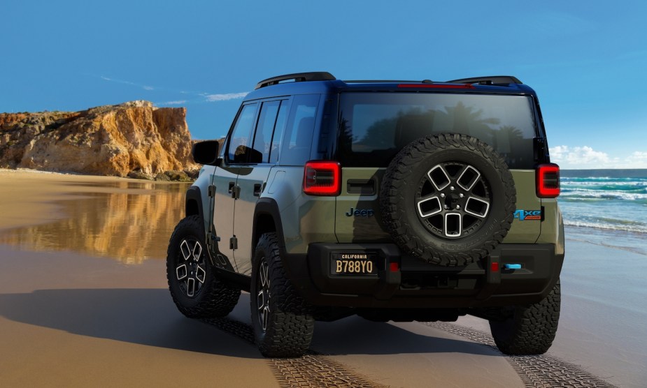 The rear of an all-new Jeep SUV parked on the beach, the ocean visible beyond it.