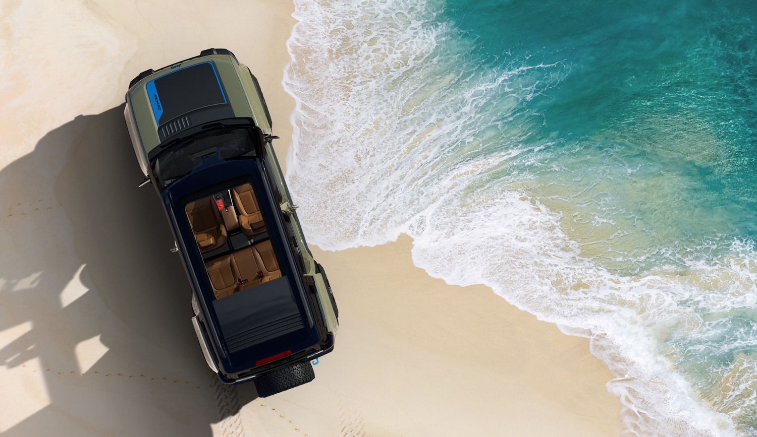 Birds-eye view of a Jeep Recon 4x4 SUV EV parked on a beach by the ocean.