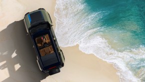 Birds-eye view of a Jeep Recon 4x4 SUV EV parked on a beach by the ocean.