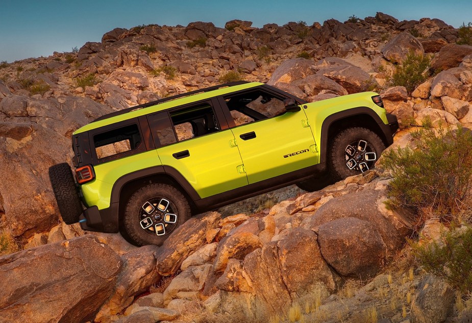 Neon green electric Jeep SUV climbing a rocky off-road trail, a mountain peak visible in the background.