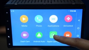 A person selecting Apple CarPlay on an infotainment system, with a potential Apple CarPlay wireless adaptor. .