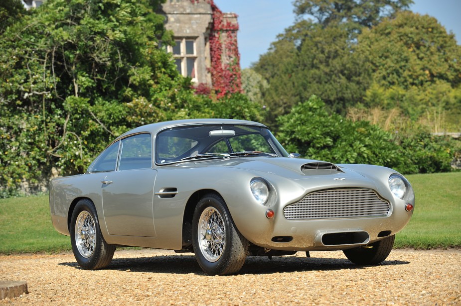 Silver Aston Martin DB4 GT parked in front of a countryside estate.