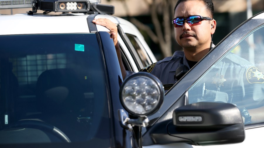 A police officer stands next to his SUV interceptor with its rooftop ALPR scanning camera.