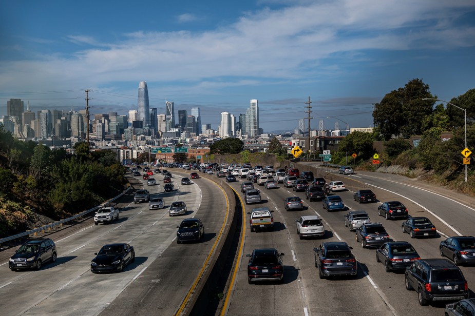 Crowded highway traffic approaches San Francisco, the city's skyline visible in the background.