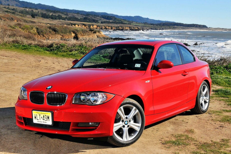 A red BMW 128i sits on a coastline road.