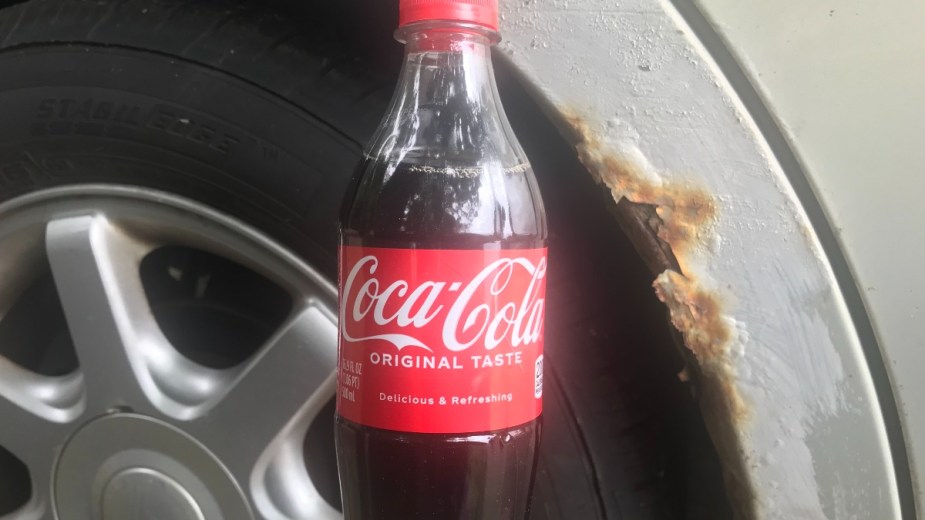 Bottle of Coca-Cola by rust spot, highlighting if Coke can remove rust from car