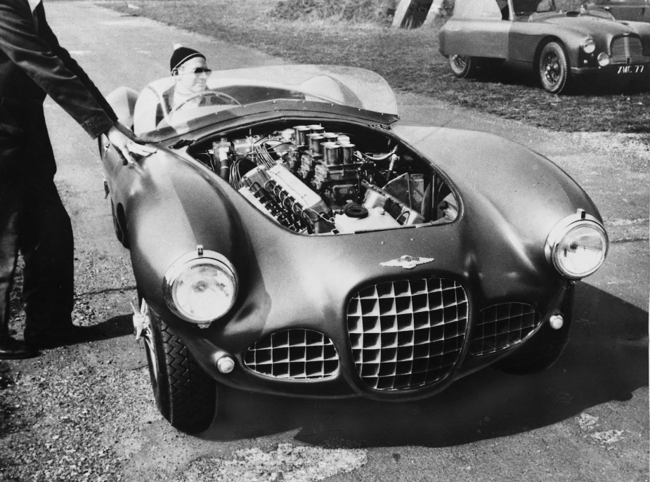 David Brown testing out a Lagonda race car with its hood removed and V12 engine exposed.
