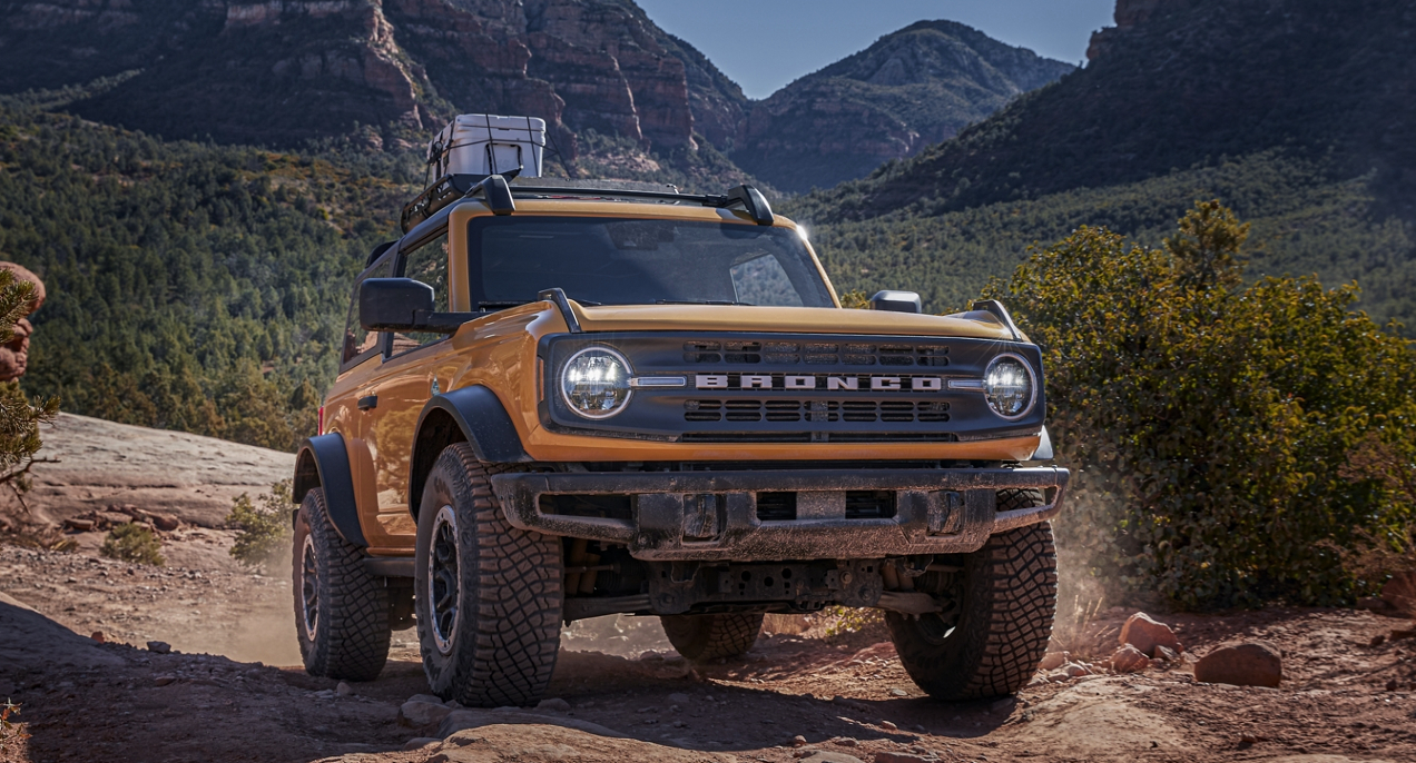 A yellow Ford Bronco midsize SUV is driving off-road. 