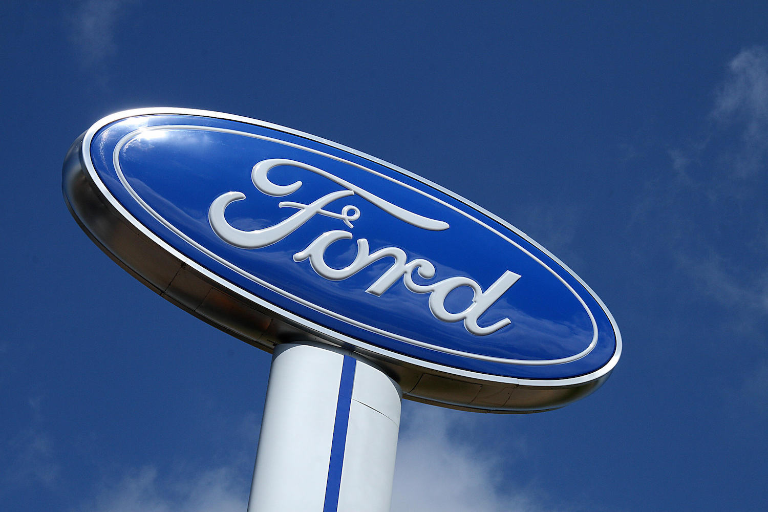 The blue Ford logo as it appears on a large sign above a dealership, the sky visible in the background.