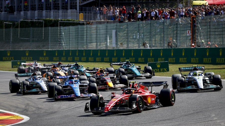A pack of 2022 Formula 1 race cars rounding a corner during the Belgium Grand Prix, the audience visible in the background.