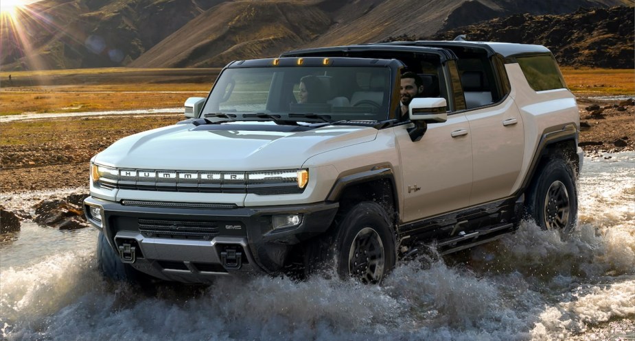 A white GMC Hummer EV is driving in shallow water. 