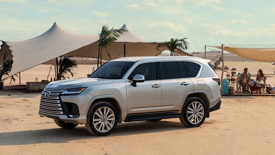 Silver Lexus LX600 full-size SUV parked in front of some tents for a publicity photo, the desert visible behind it.