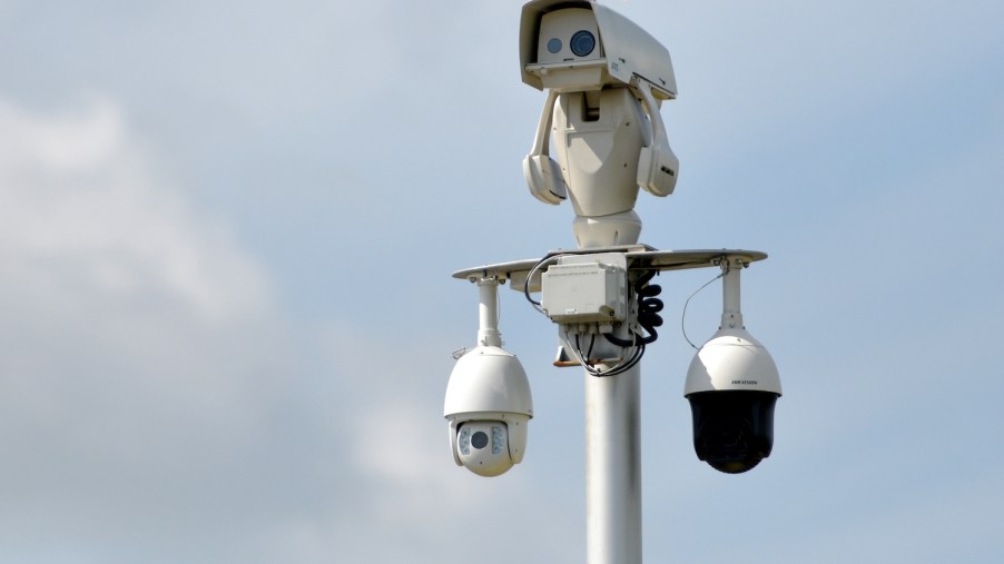 The scanners of an automatic license reader system mounted high on a pole over a highway, the sky visible in the background.