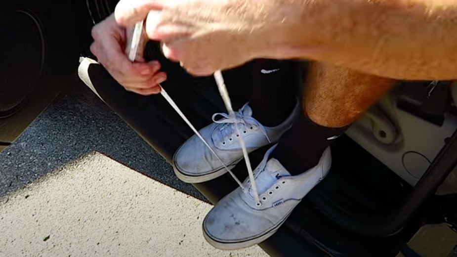 Man removing shoelace strings from shoes to unlock car door of SUV