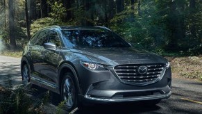 A gray 2023 Mazda CX-9 midsize SUV is driving on the road.