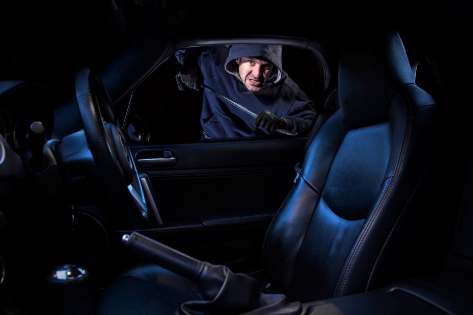 A man breaking into a parked car at night. 