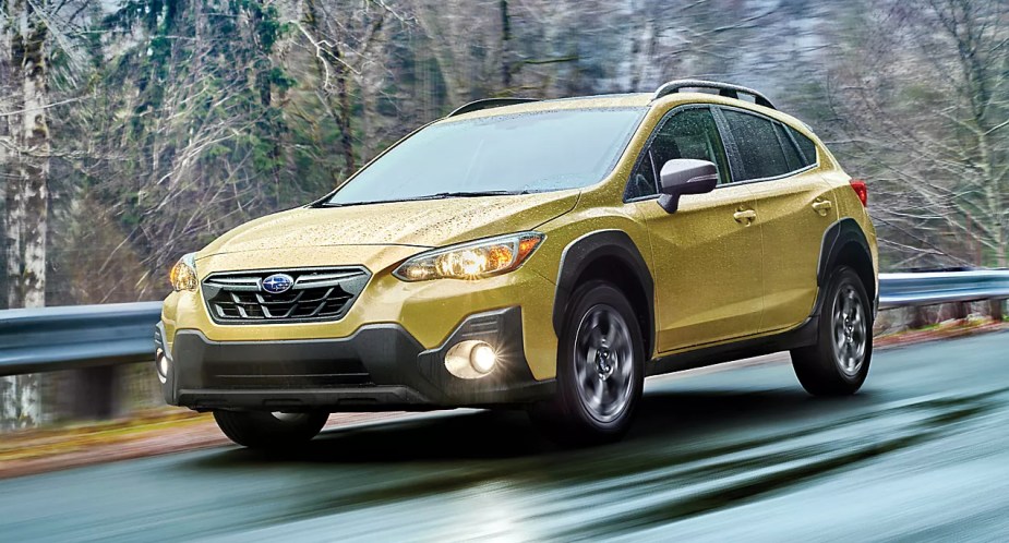 A yellow 2023 Subaru Crosstrek subcompact SUV is driving on a wet road. 