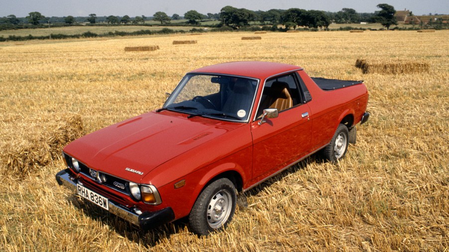 A red Subaru Brat sits in an open field as a vintage ute.