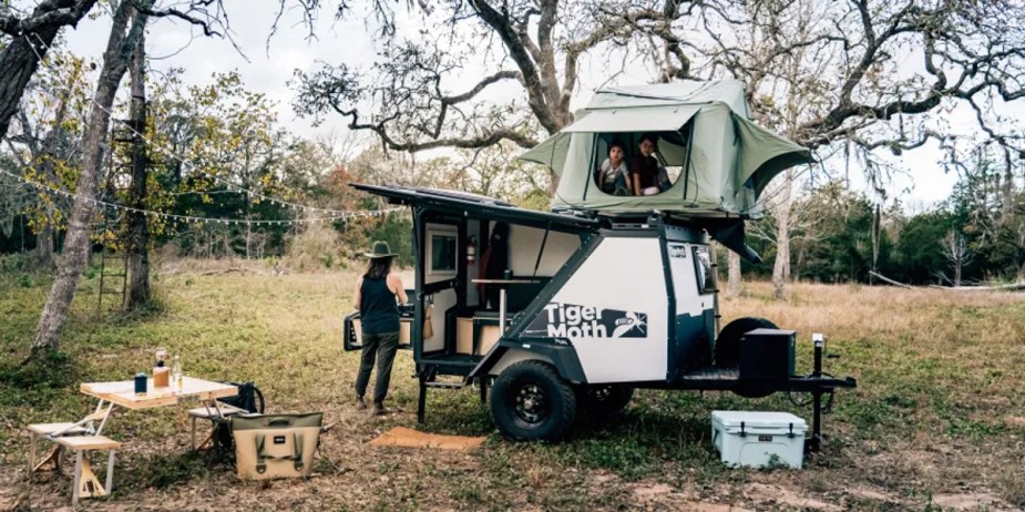 Taxa's trailer camper sits in a wooded area, showing off its functionality while camping.