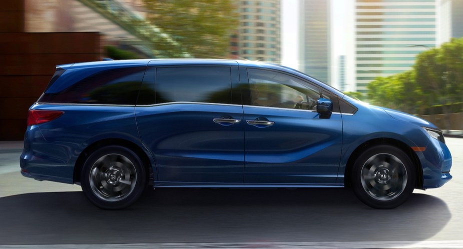 A blue Honda Odyssey minivan is driving on the road. 