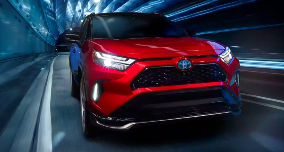 A red 2022 Toyota RAV4 Prime small plug-in hybrid SUV is driving.