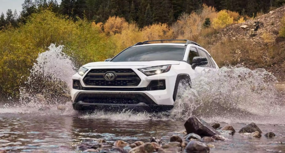 A white 2022 Toyota RAV4 small SUV is driving through the water. 