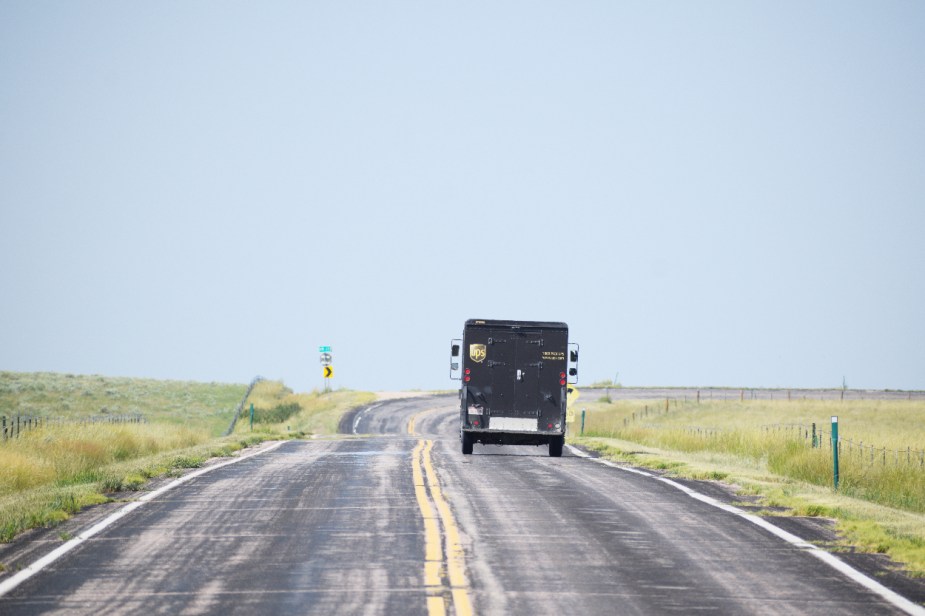 The rear-end of a UPS Package Car as it drives down a remote road.