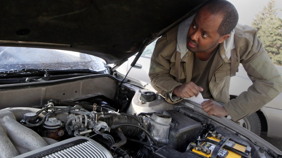 A person looking under the hood where a potentially dirty engine is.