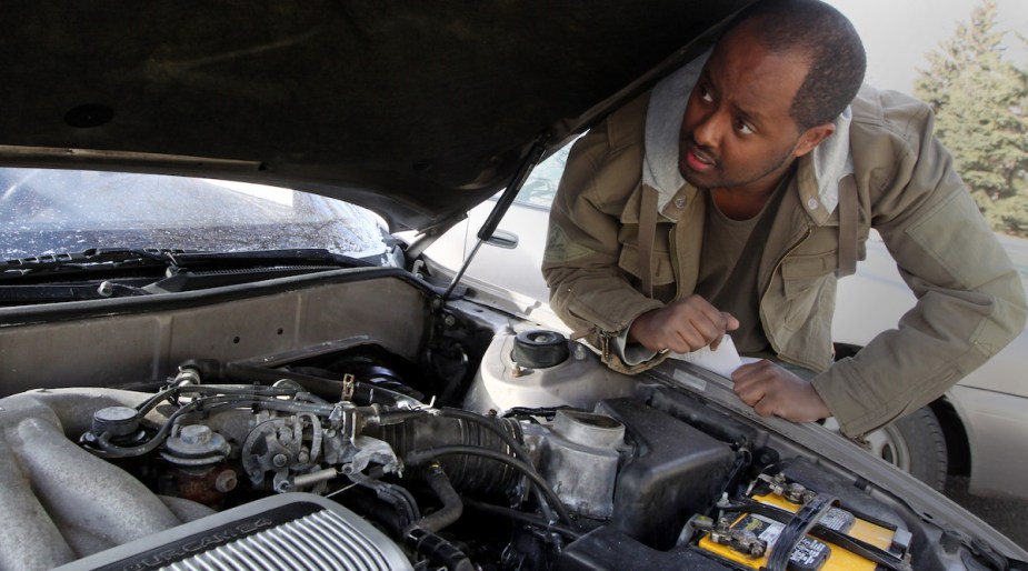 A person looking under the hood where a potentially dirty engine is.