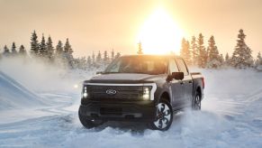 A 2022 Ford F-150 Lightning electric truck driving on snow with its headlights on as the sun sets in Alaska