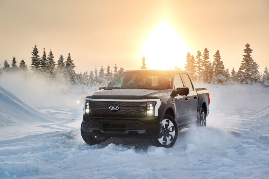 A 2022 Ford F-150 Lightning electric truck driving on snow with its headlights on as the sun sets in Alaska
